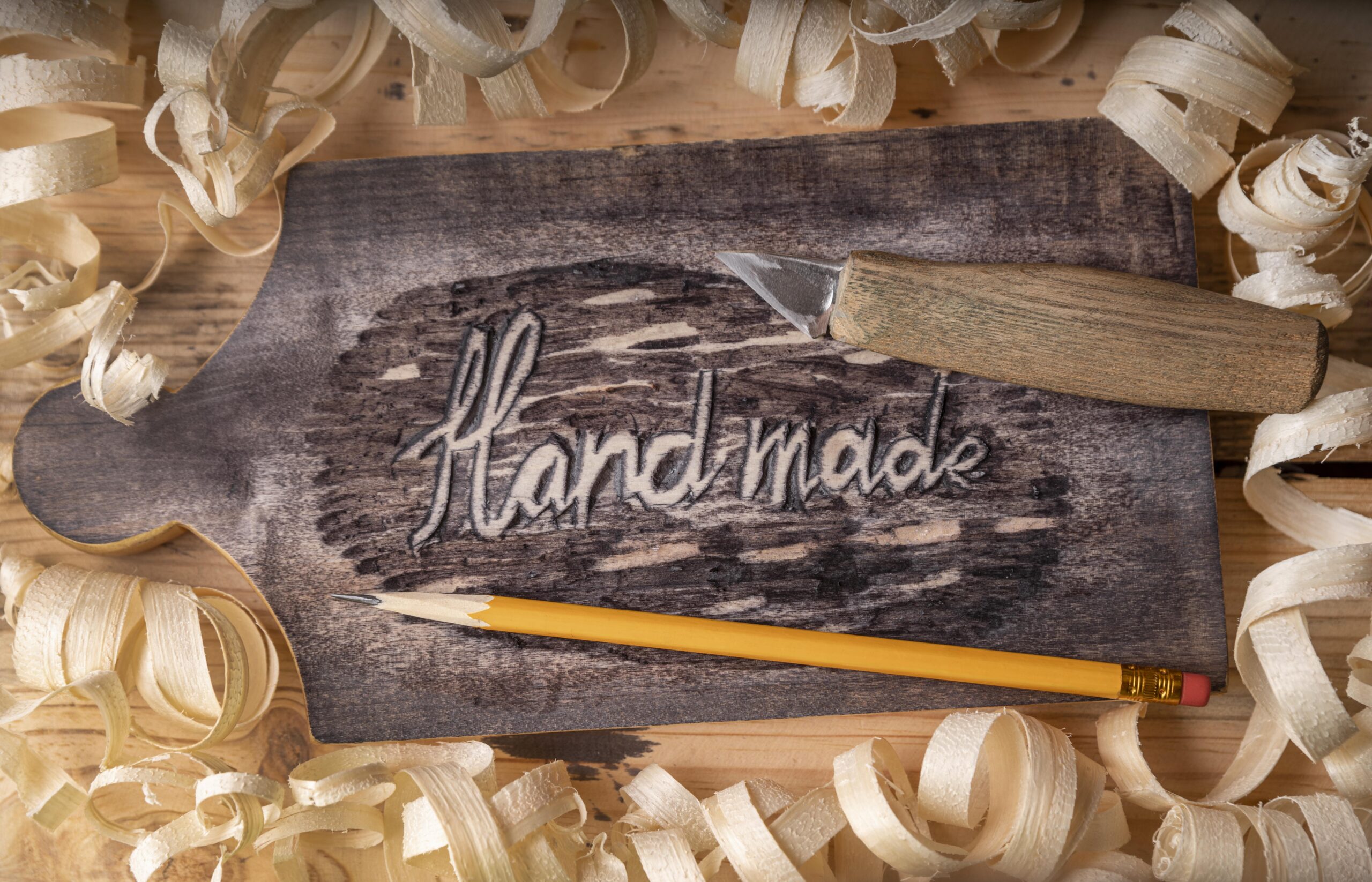 Holzpaddle mit der Gravur „Handmade“, Schnitzwerkzeug und Holzspänen – Symbol für einen sexpositiven Workshop zum Holzpaddle-Schnitzen in Stuttgart.