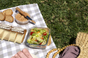 Picknickdecke mit Snacks, Brot, Käse und Salat auf einer Wiese als Symbol für gemeinsames Essen beim sexpositiven Picknick.