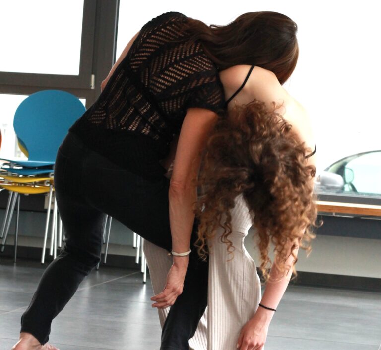 Zwei Frauen bewegen sich in einer improvisierten Tanzbewegung miteinander in einem hellen Raum.