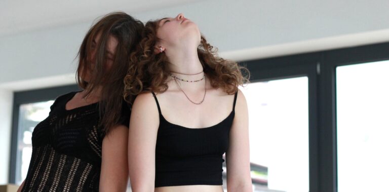 Zwei Frauen stehen Rücken an Rücken und bewegen sich langsam miteinander.